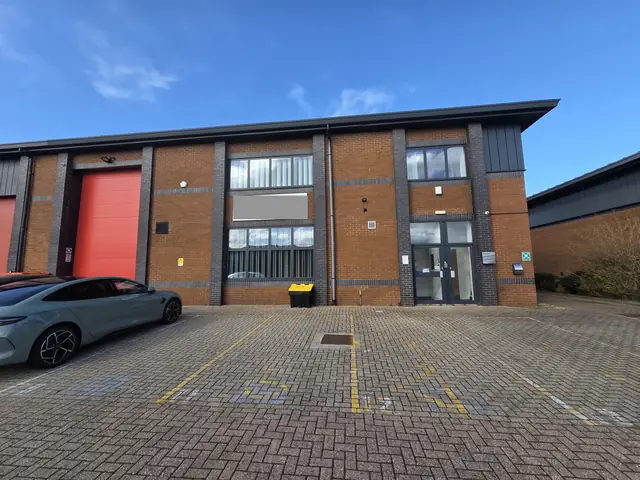 Front elevation of a two-storey brick-built industrial and office unit with a red roller shutter door and glazed entrance