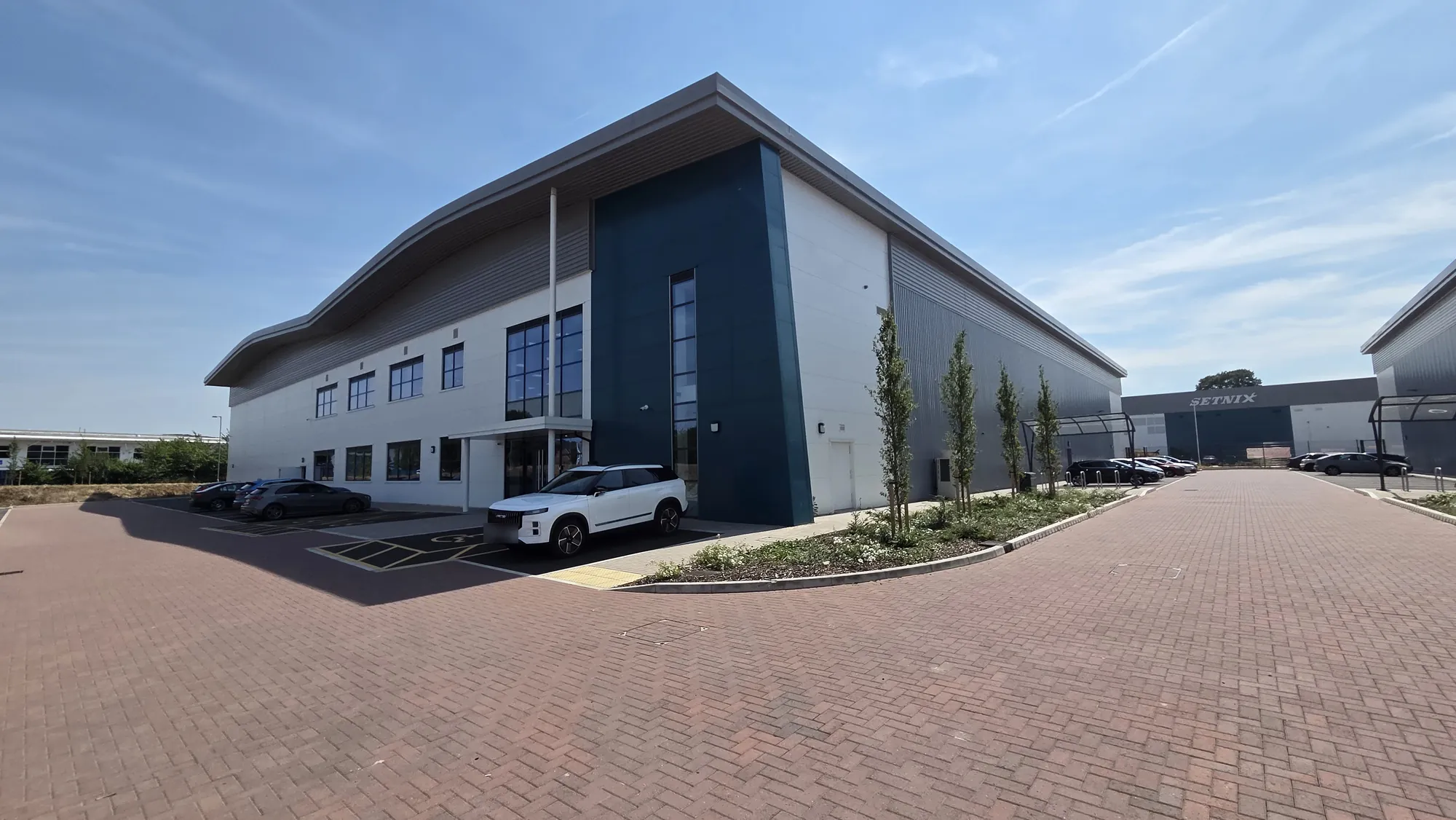Corner view of a modern two-storey office wing and warehouse unit with white and teal cladding and a curved roof