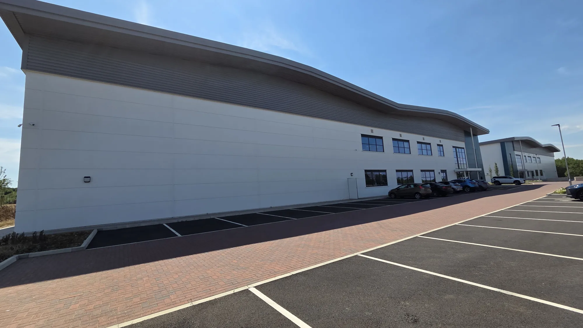 Long side elevation of the modern warehouse unit with a curved roof line and car park alongside