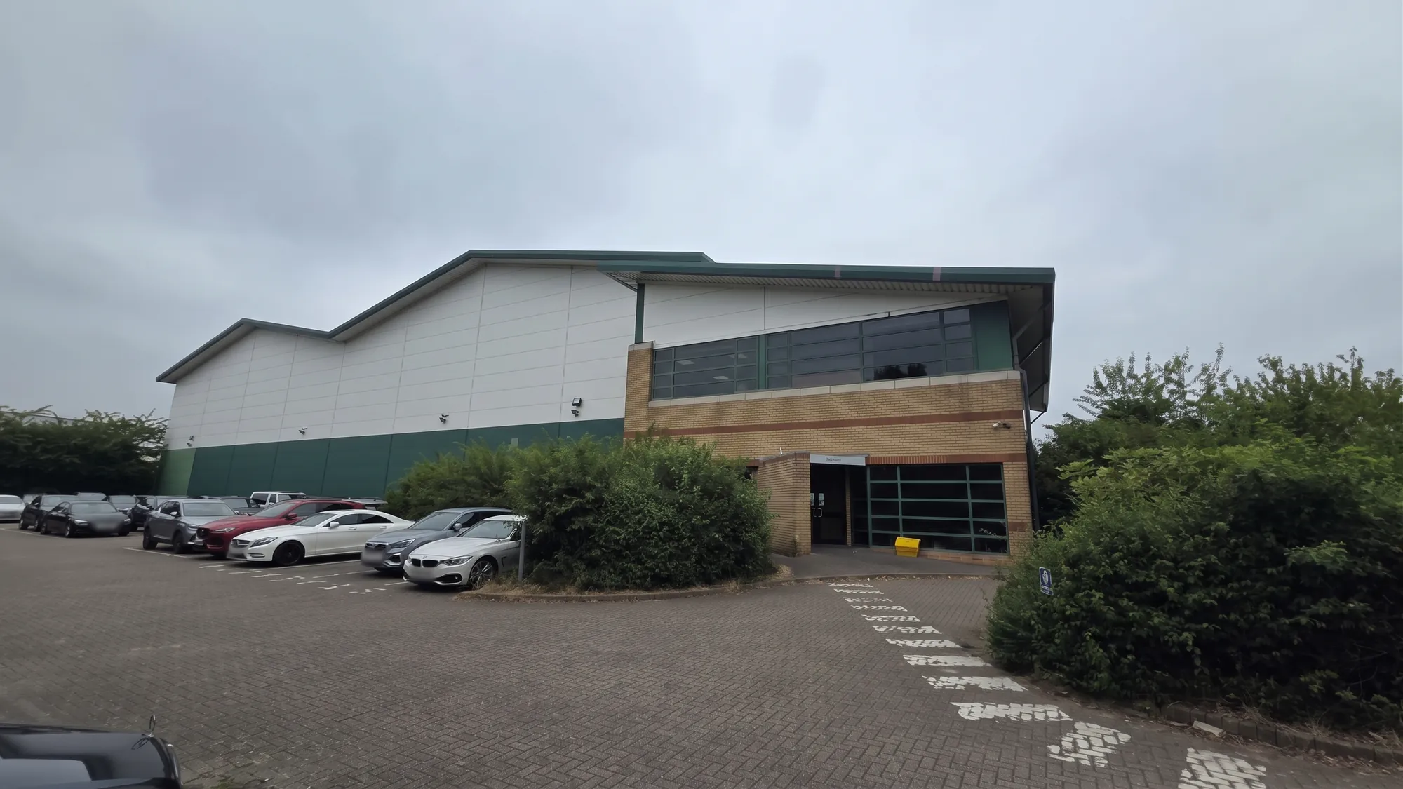Entrance and office wing of a large industrial warehouse unit with green and white cladding and a car park in front